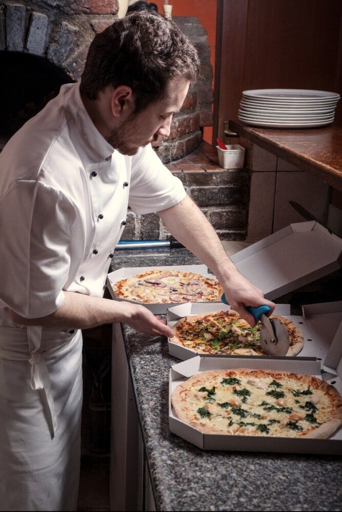 Kuchař zakládá pizzu do rozehřáté pece na dřevo